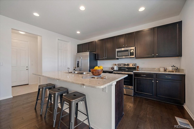 kitchen featuring a breakfast bar, dark wood-style flooring, appliances with stainless steel finishes, a sink, and an island with sink