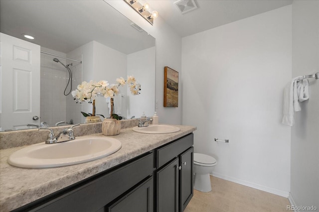 bathroom featuring toilet, tiled shower, a sink, and visible vents