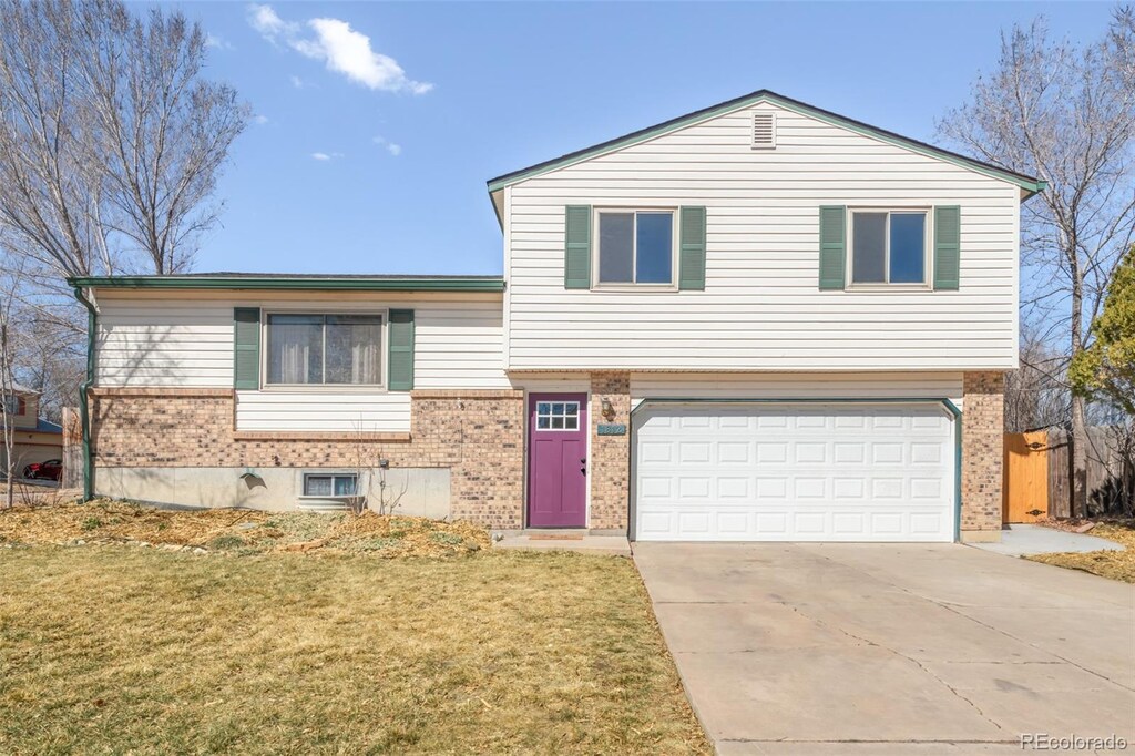split level home with brick siding, an attached garage, concrete driveway, and a front yard