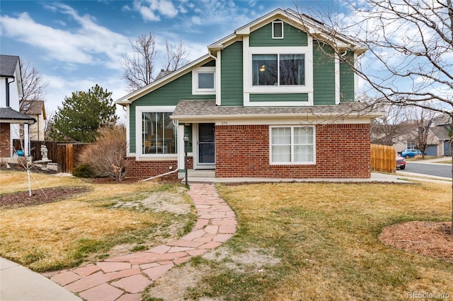 view of front facade with brick siding, roof with shingles, a front lawn, and fence