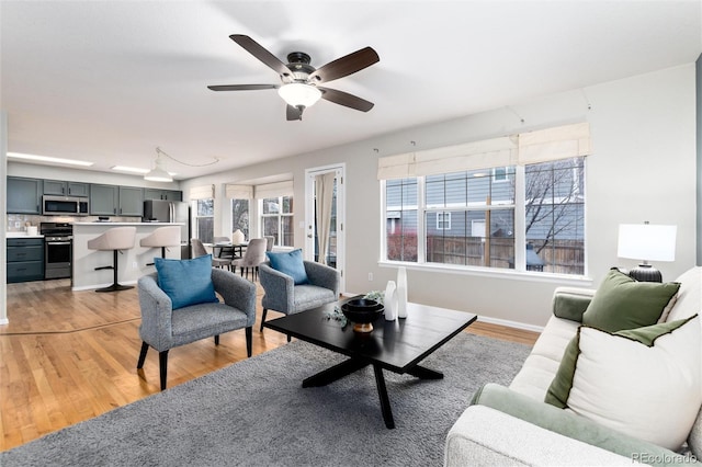 living area with baseboards, light wood finished floors, and ceiling fan