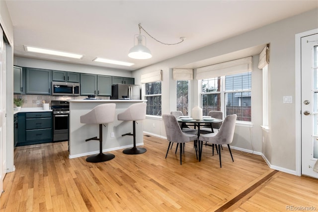 kitchen featuring baseboards, light wood-style flooring, light countertops, appliances with stainless steel finishes, and a kitchen breakfast bar