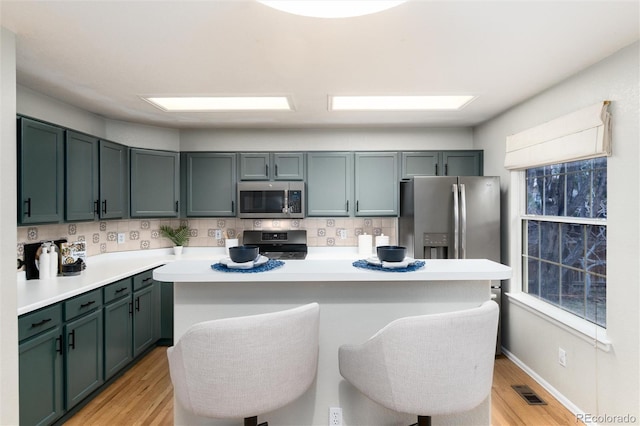 kitchen with visible vents, a kitchen island, light wood-style flooring, stainless steel appliances, and light countertops