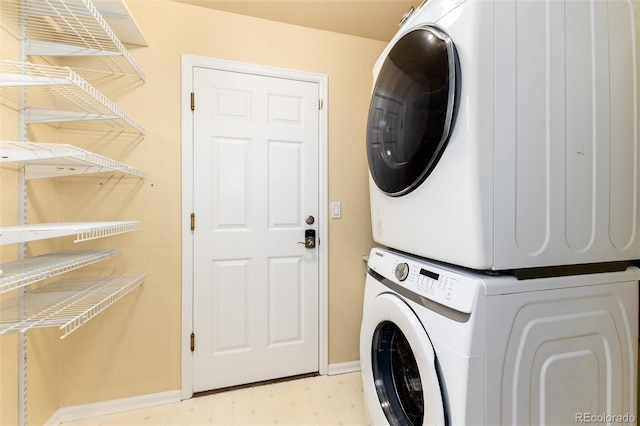 clothes washing area featuring baseboards, light floors, laundry area, and stacked washer / dryer