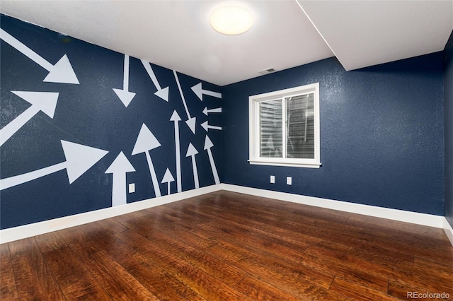 spare room with hardwood / wood-style flooring, visible vents, baseboards, and a textured wall