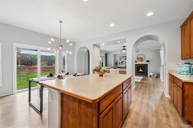6723 Silverwind Cir, Colorado Springs, CO 80923 - kitchen featuring brown cabinets, light wood-style flooring, a kitchen island, light countertops, and a warm lit fireplace
