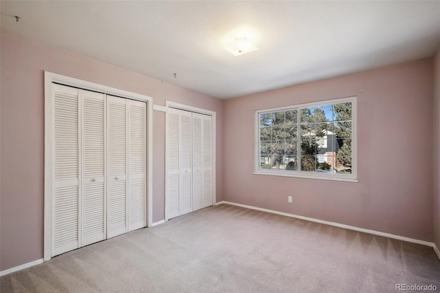 unfurnished bedroom featuring two closets and light carpet