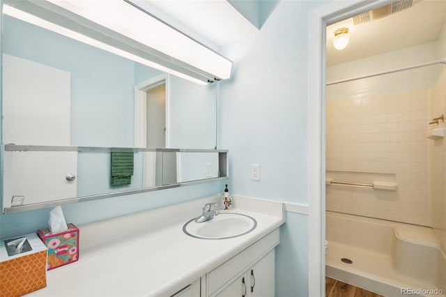 bathroom featuring a tile shower, vanity, toilet, and hardwood / wood-style floors