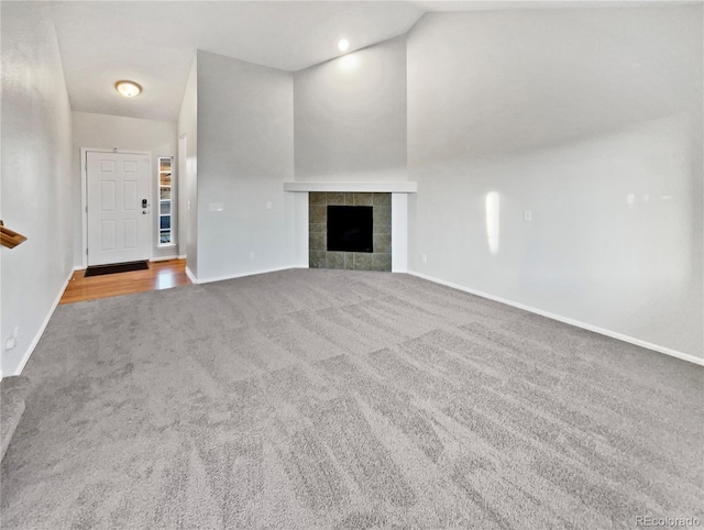 unfurnished living room with carpet floors, a tile fireplace, lofted ceiling, and baseboards