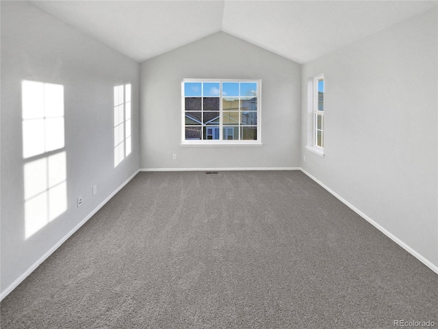 spare room with lofted ceiling, dark carpet, and baseboards