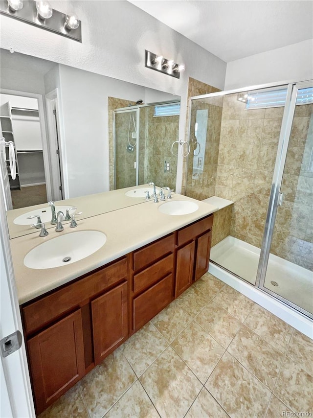 bathroom featuring double vanity, a shower stall, a spacious closet, and a sink