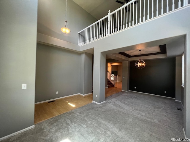 unfurnished living room with a chandelier, wood-type flooring, a towering ceiling, and a tray ceiling