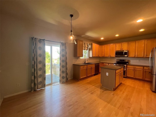 kitchen featuring hanging light fixtures, sink, light wood-type flooring, appliances with stainless steel finishes, and a kitchen island