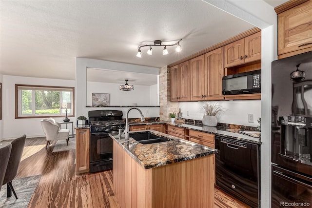 1060 S Eaton St, Lakewood, CO 80226 - kitchen with black appliances, wood finished floors, dark stone counters, an island with sink, and a textured ceiling
