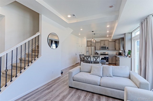 living room featuring light wood-type flooring, an inviting chandelier, and sink