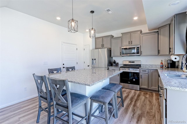 kitchen with a center island, a breakfast bar area, stainless steel appliances, hardwood / wood-style floors, and decorative light fixtures