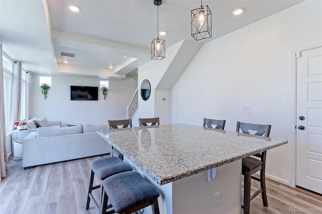 kitchen featuring light wood-type flooring, a tray ceiling, decorative light fixtures, and a breakfast bar area