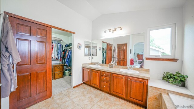 9832 N Crystal Lake Dr, Littleton, CO 80125 - bathroom featuring double vanity, vaulted ceiling, a relaxing tiled tub, a walk in closet, and ensuite bathroom