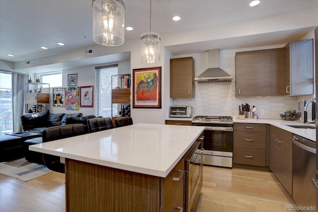 kitchen featuring light countertops, light wood-style flooring, stainless steel appliances, wall chimney exhaust hood, and a sink