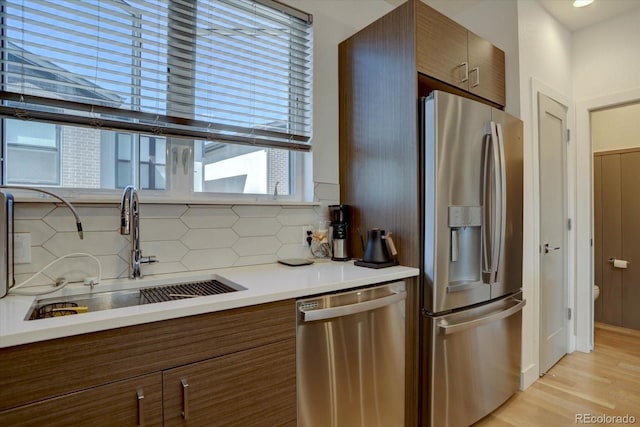 kitchen featuring tasteful backsplash, light countertops, light wood-style floors, stainless steel appliances, and a sink