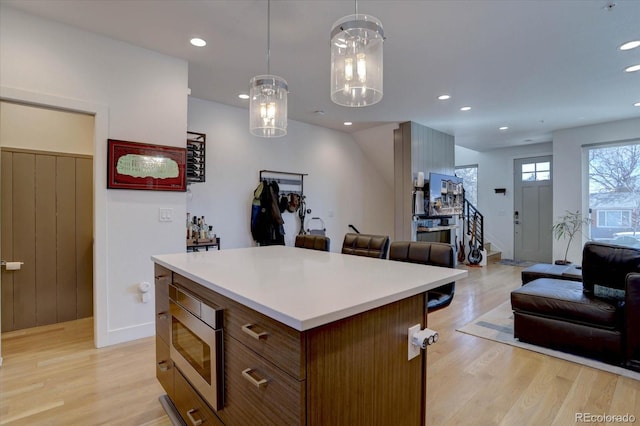 kitchen featuring stainless steel microwave, light countertops, open floor plan, and light wood finished floors