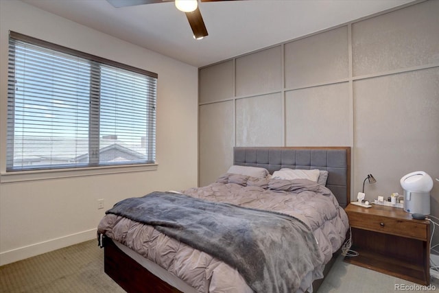 bedroom featuring baseboards, light colored carpet, a ceiling fan, and a decorative wall