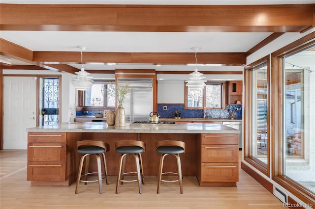 kitchen with backsplash, beamed ceiling, light wood-type flooring, appliances with stainless steel finishes, and a sink