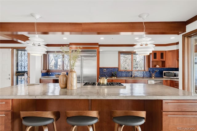 kitchen featuring tasteful backsplash, light countertops, brown cabinets, appliances with stainless steel finishes, and a notable chandelier