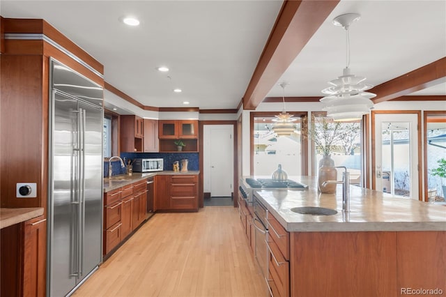 kitchen with a sink, beamed ceiling, appliances with stainless steel finishes, and brown cabinetry