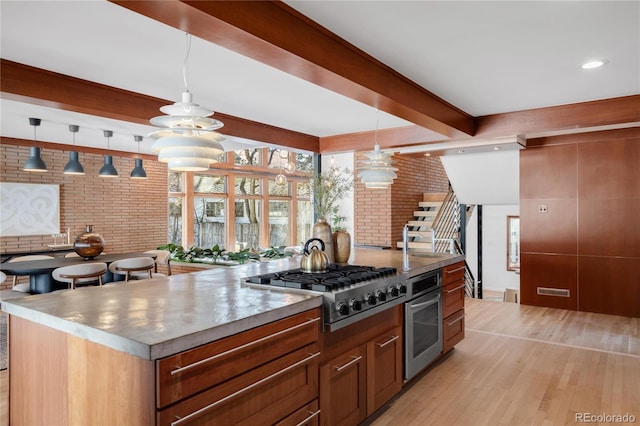 kitchen with brick wall, beam ceiling, stainless steel appliances, hanging light fixtures, and light wood-style floors