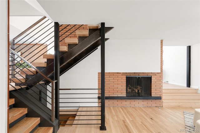 staircase with a fireplace, wood finished floors, and visible vents