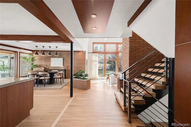 foyer with stairs, beam ceiling, light wood-style flooring, and brick wall