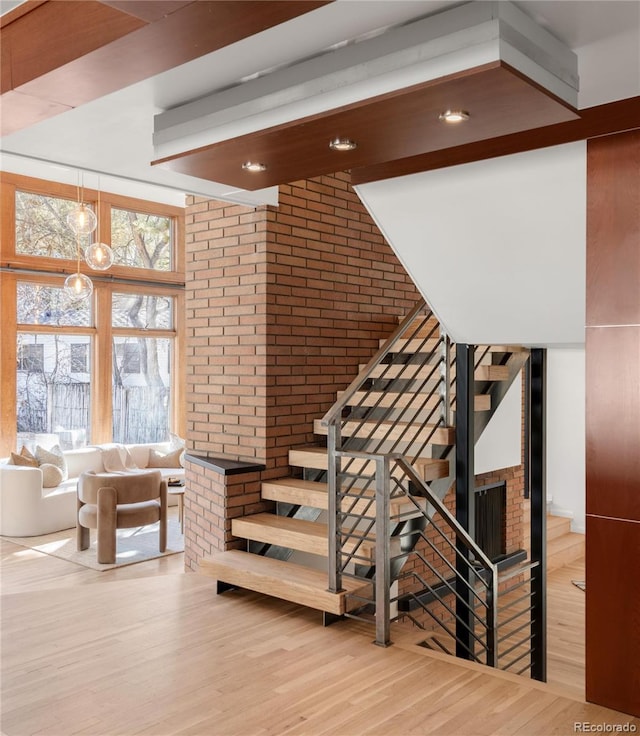 staircase with beam ceiling, a brick fireplace, wood finished floors, and brick wall