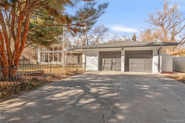 exterior space with fence, roof with shingles, concrete driveway, an outdoor structure, and a garage