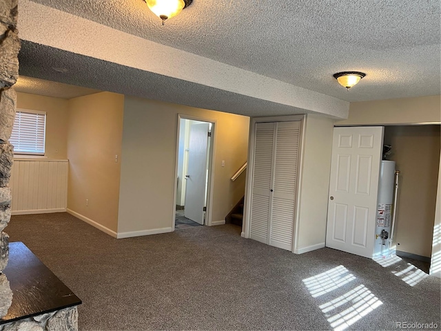 basement featuring water heater, a textured ceiling, and dark colored carpet