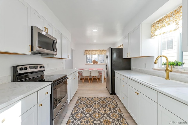 kitchen with light stone countertops, appliances with stainless steel finishes, sink, light hardwood / wood-style flooring, and white cabinetry