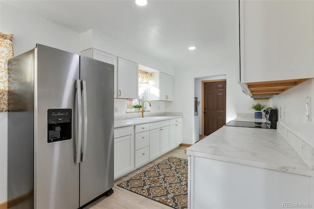 kitchen with sink, stainless steel refrigerator with ice dispenser, light hardwood / wood-style flooring, light stone countertops, and white cabinetry