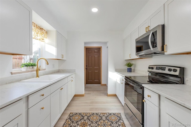 kitchen with light stone countertops, sink, stainless steel appliances, white cabinets, and light wood-type flooring