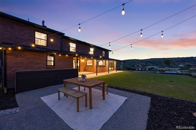 patio terrace at dusk featuring a mountain view, a lawn, and a garage