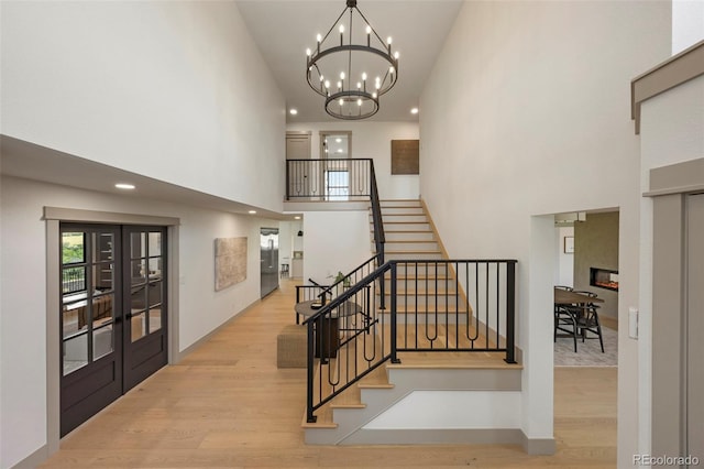 stairs featuring a high ceiling, a notable chandelier, hardwood / wood-style flooring, and french doors