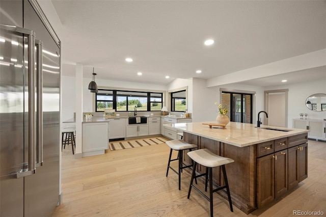 kitchen with sink, light wood-type flooring, stainless steel built in refrigerator, white cabinets, and a center island with sink