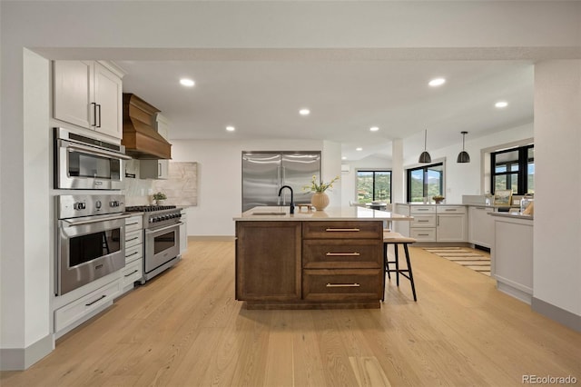 kitchen with a center island with sink, a breakfast bar area, custom range hood, pendant lighting, and stainless steel appliances