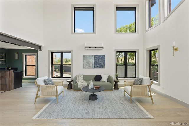 living room featuring a wall mounted AC, a high ceiling, and light hardwood / wood-style flooring