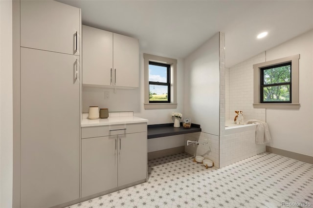 bathroom featuring vanity, a relaxing tiled tub, and vaulted ceiling