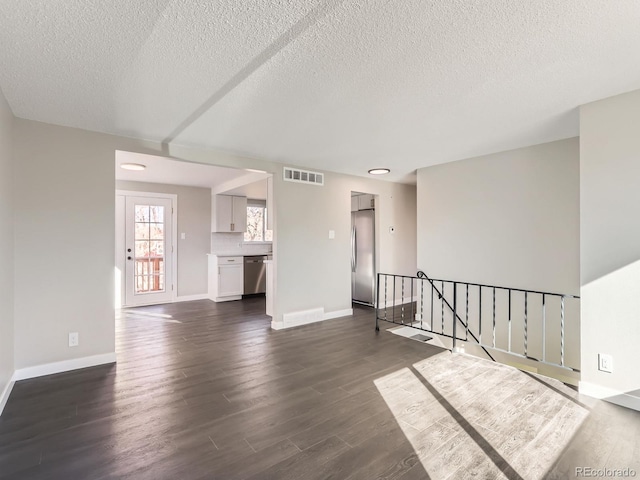 spare room with a textured ceiling, visible vents, dark wood-style flooring, and baseboards