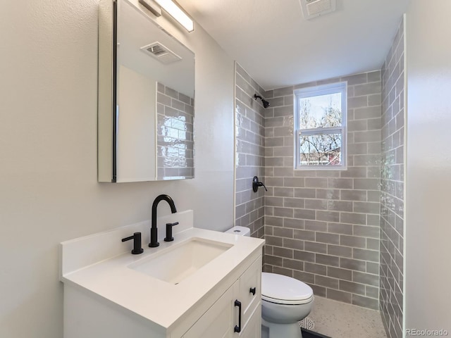 bathroom featuring a tile shower, visible vents, toilet, and vanity