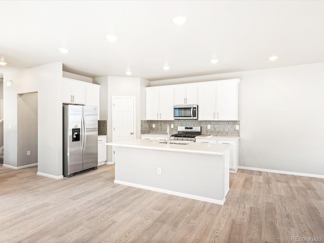 kitchen featuring light wood finished floors, stainless steel appliances, light countertops, backsplash, and a kitchen island with sink