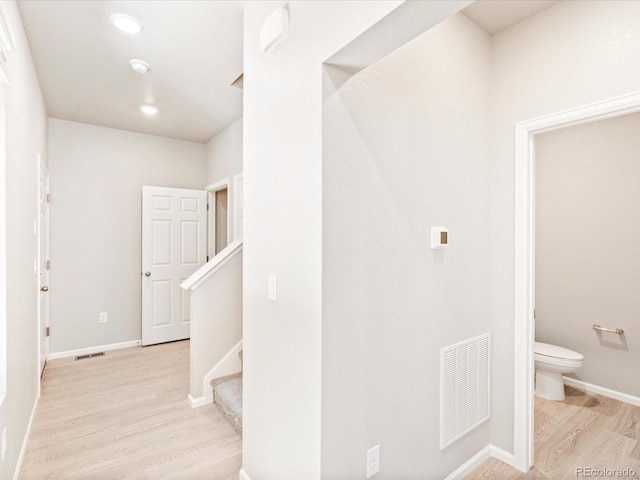 corridor with light wood-style flooring, stairs, visible vents, and baseboards