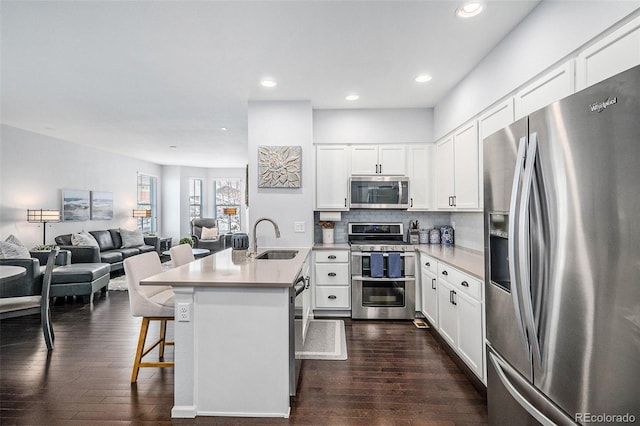 kitchen with white cabinets, a breakfast bar, open floor plan, stainless steel appliances, and light countertops