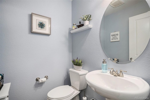 half bathroom featuring toilet, visible vents, a sink, and a textured wall